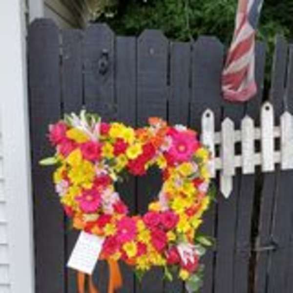 Heart-shaped floral wreath on a fence with bright pink, yellow, and orange flowers
