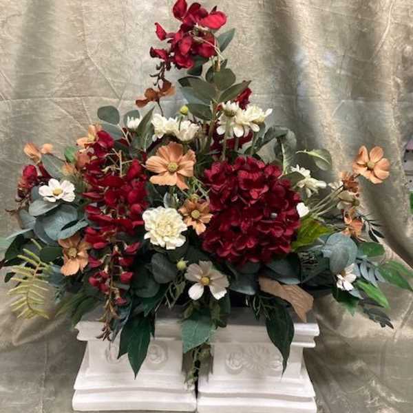 Red and peach floral arrangement in a white pedestal container