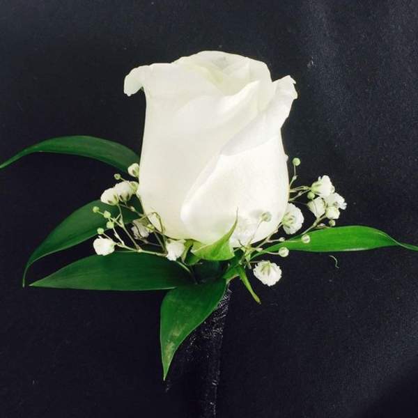 White rose boutonniere with small white filler flowers and green leaves