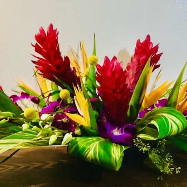 Tropical flower arrangement with red, purple, and yellow blooms in a low container