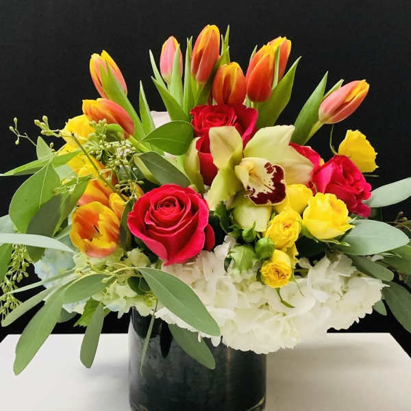 Mixed bouquet of tulips, roses, orchids, and white hydrangeas in a black vase