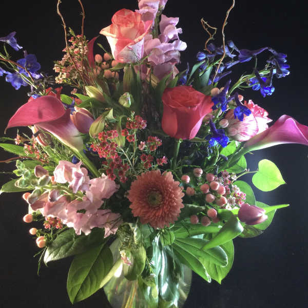 Tall mixed bouquet in a glass vase with pink, purple, and red blooms