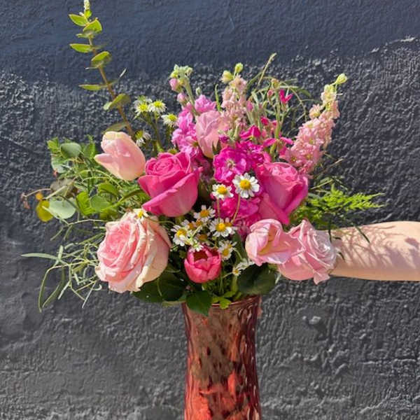Tall pink glass vase with mixed bouquet of pink roses, tulips, stock, and small white daisies.