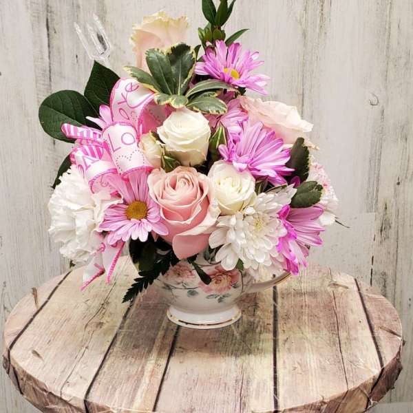 Pink and white flower arrangement in a floral teacup vase with a ribbon