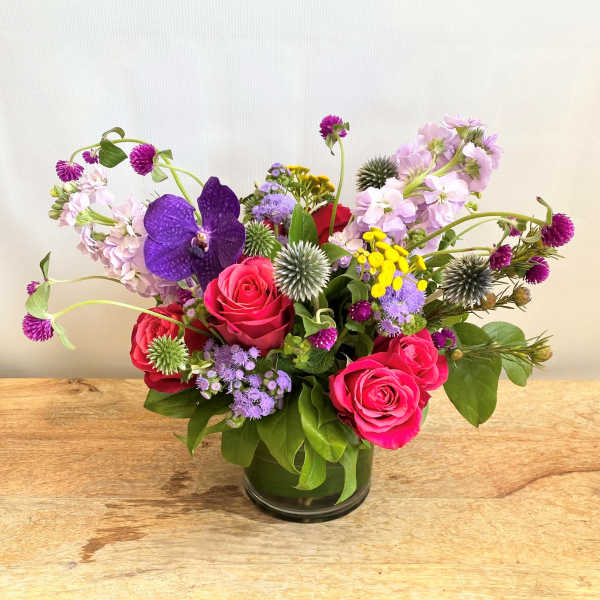 Mixed bouquet of pink roses, purple orchids, and small wildflowers in a glass vase