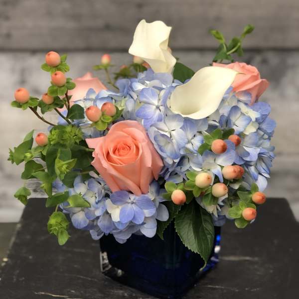 Blue hydrangeas with pink roses and white calla lilies in a dark vase