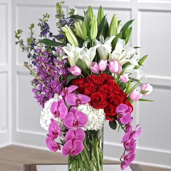 Tall bouquet of red roses, white lilies, and pink orchids in a glass vase