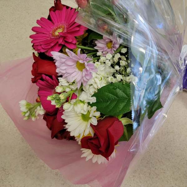 Bouquet of red roses, pink gerbera daisies, and white daisies wrapped in pink and clear plastic