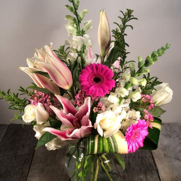 Mixed bouquet of pink lilies, white roses, and bright gerbera daisies in a glass vase