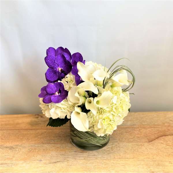 Purple orchids and white calla lilies arranged in a glass vase