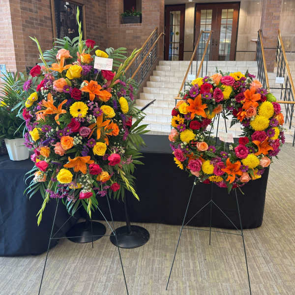 Two large floral wreaths on stands with bright mixed flowers