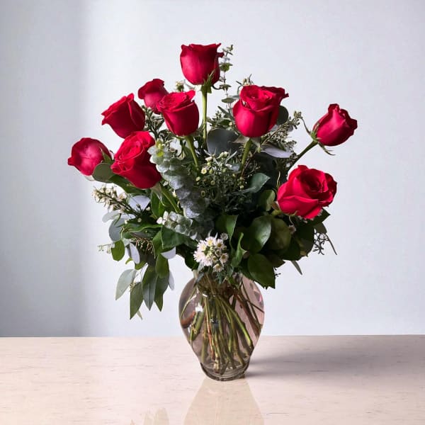 Red roses arranged in a clear glass vase with mixed greenery