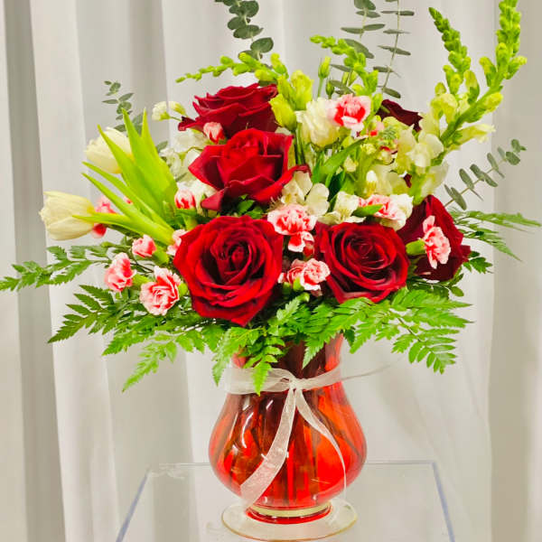 Red roses and pink carnations in a red glass vase with a white ribbon