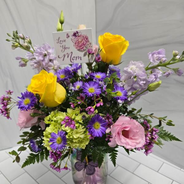 Mixed bouquet in a glass vase with yellow roses, pink blooms, and purple daisies