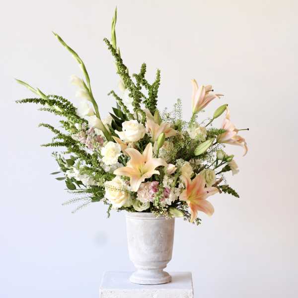 Peach lilies and white roses in a white pedestal vase