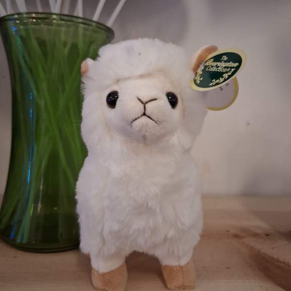 White plush alpaca toy beside a green glass vase