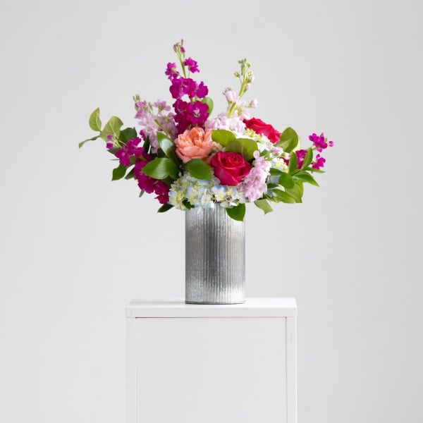 Tall mixed bouquet of pink and peach flowers with blue hydrangea in a silver metal vase