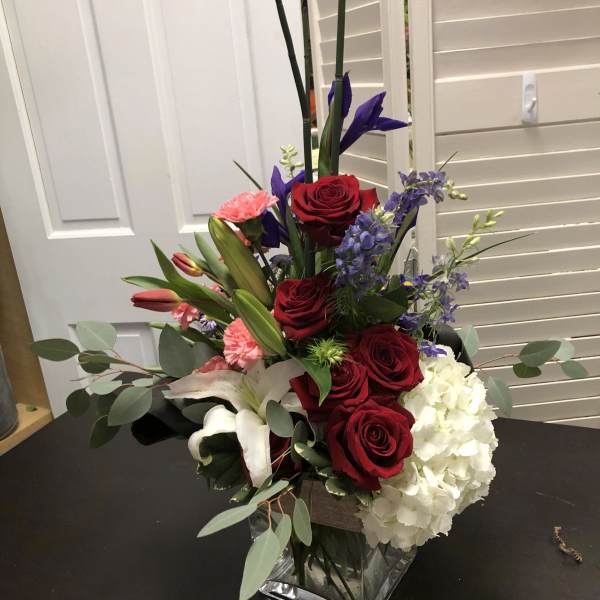 Mixed bouquet with red roses, white hydrangea, and purple flowers in a square glass vase