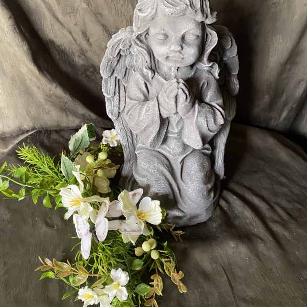 Gray praying angel statue with a small white floral garland