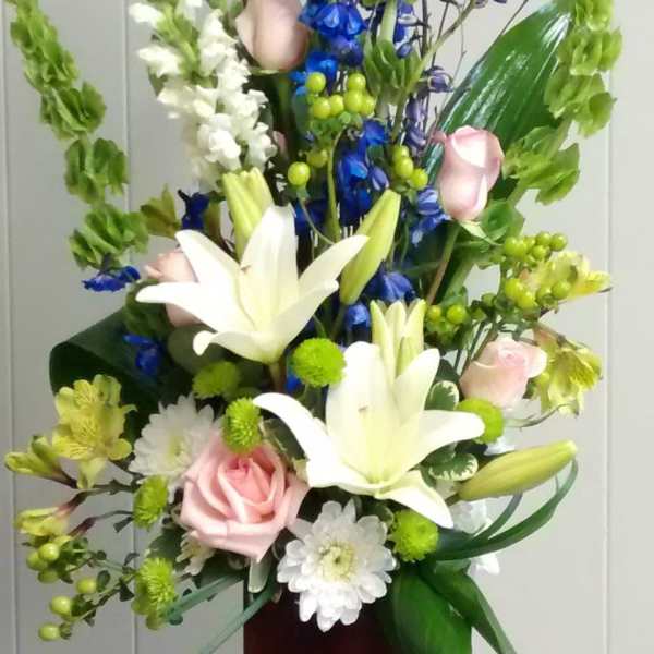 Tall floral arrangement with white lilies, pink roses, and blue flowers in a wooden vase