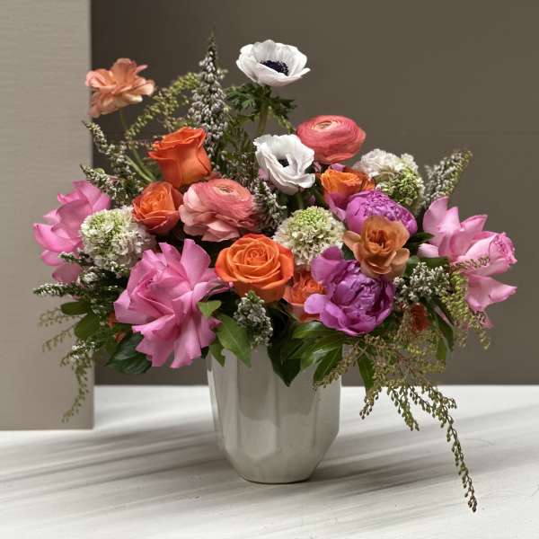 Mixed pink, orange, and white flowers arranged in a white vase