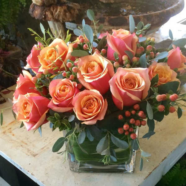 Low arrangement of peach and pink roses in a clear glass cube vase