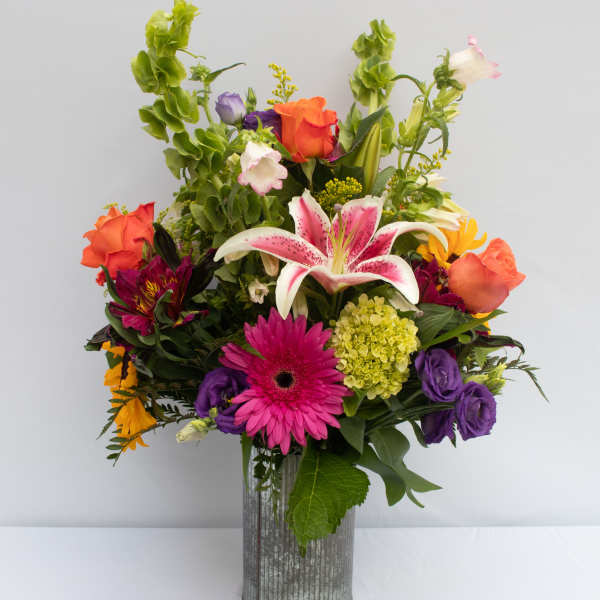 Colorful mixed bouquet in a clear glass vase with lilies, roses, and gerbera daisies