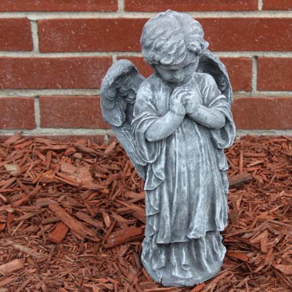 Gray angel statue with folded hands in front of a brick wall