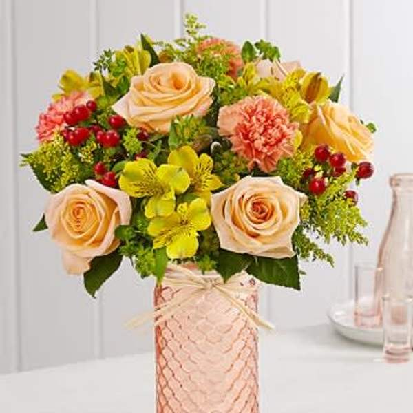 Peach roses and yellow flowers arranged in a pink glass vase
