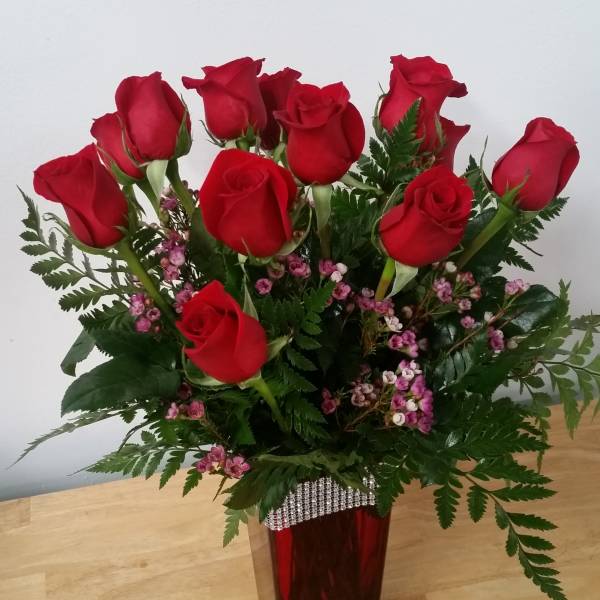 Red roses arranged in a tall vase with pink filler flowers