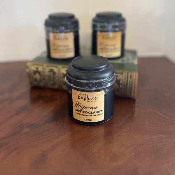 Black tea tin with gold label on a wood surface, with two similar tins blurred behind on stacked books.