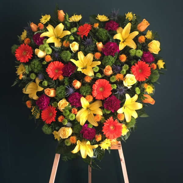 Heart-shaped floral spray with yellow lilies and mixed bright blooms on an easel