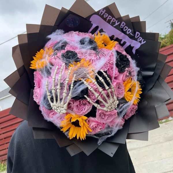 Halloween bouquet with pink roses, yellow flowers, spiderwebs, and skeleton hands
