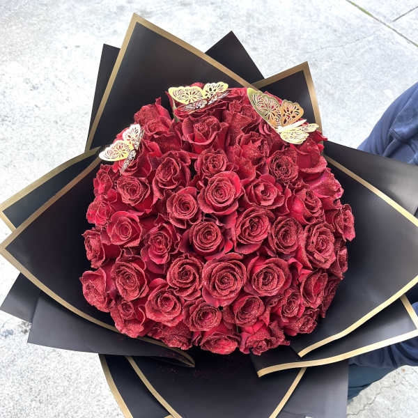 A round bouquet of red roses wrapped in black paper with gold trim