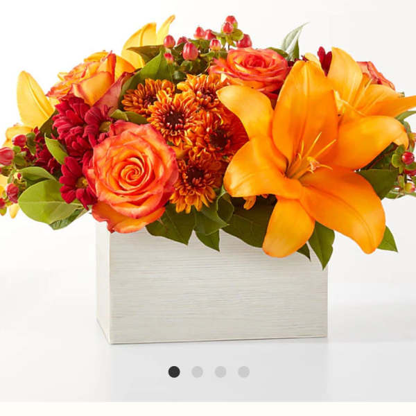 Orange and red floral arrangement in a square white box