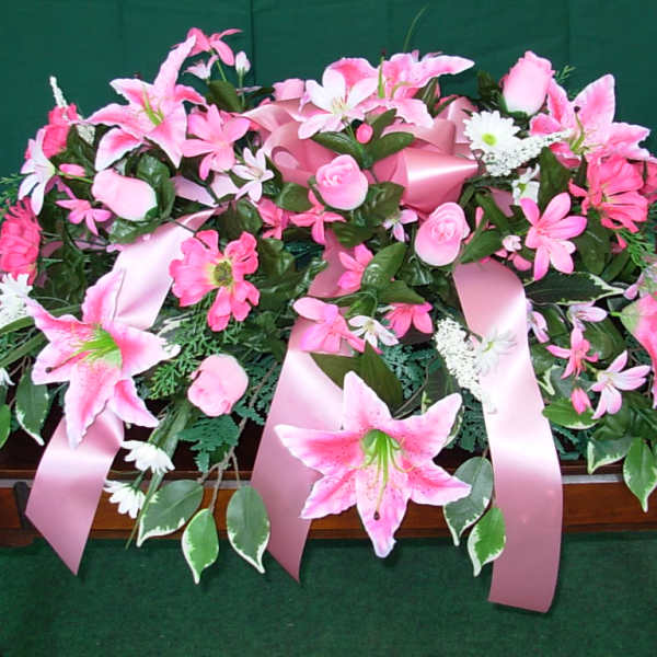 Pink floral casket spray with lilies and roses on a dark surface