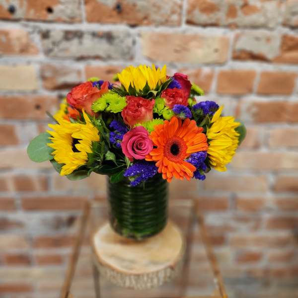 Colorful bouquet with sunflowers, roses, and a gerbera daisy in a glass vase