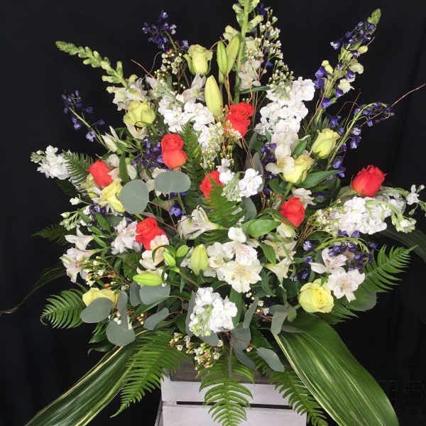 Large mixed floral arrangement with red and yellow roses in a white crate