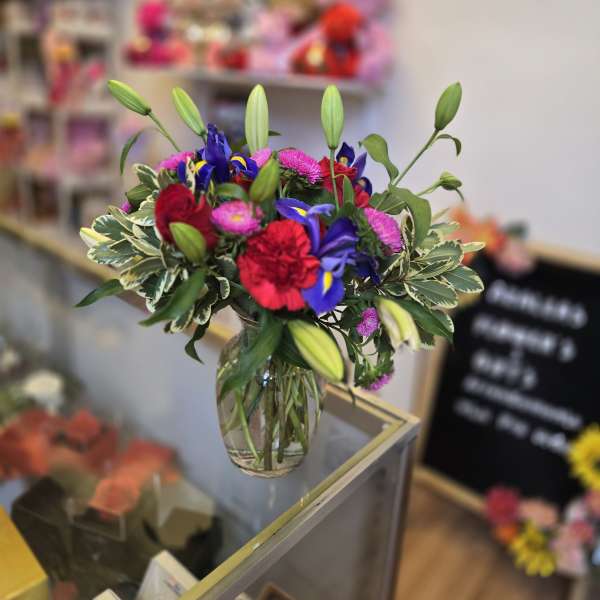 Mixed bouquet in a clear glass vase with lilies, roses, and purple blooms