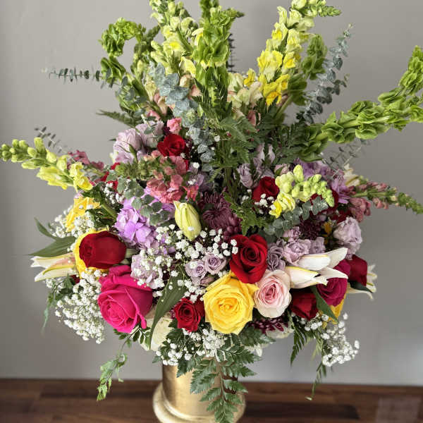 Large mixed flower arrangement in a gold pedestal vase