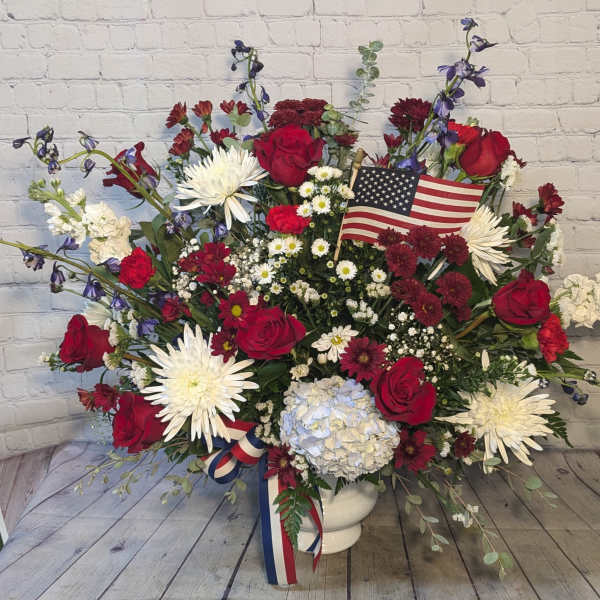 Large red, white, and blue floral arrangement in a white vase with an American flag