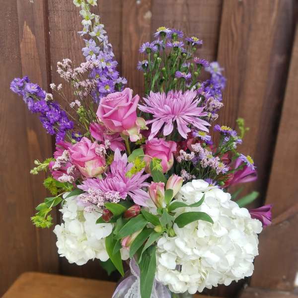 Pink roses and purple flowers arranged in a glass vase with white hydrangeas