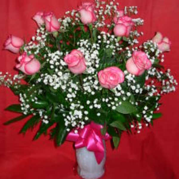 Pink roses and baby's breath in a white vase with a pink ribbon