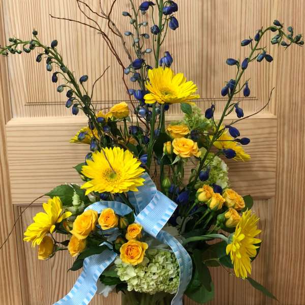 Yellow gerberas and roses in a glass vase with blue ribbon accents