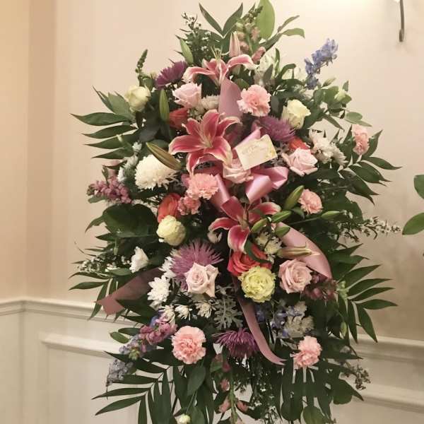Standing floral spray with pink lilies, roses, and carnations on an easel