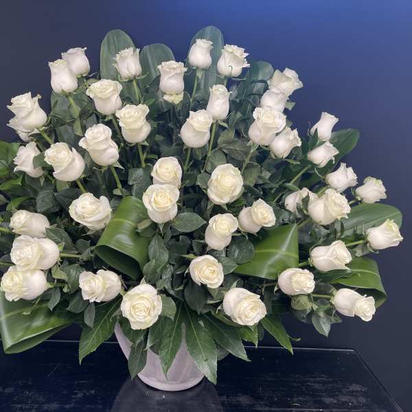White roses arranged in a vase with broad green leaves