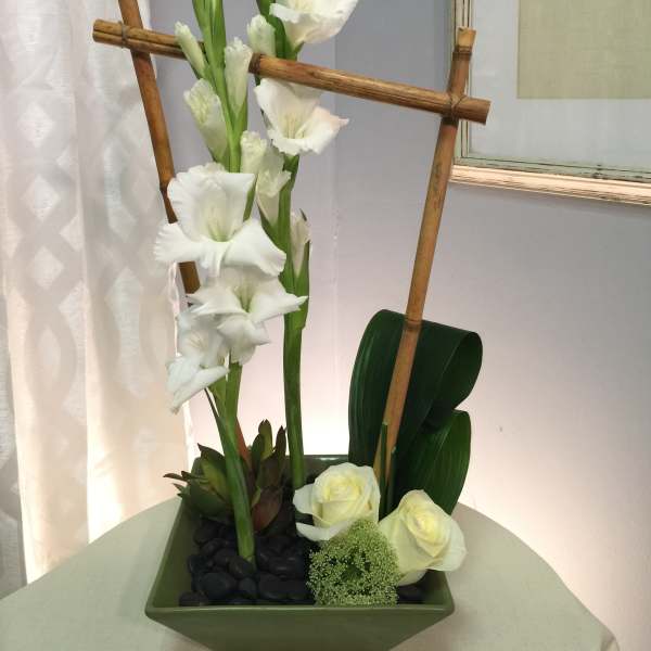 Tall white gladiolus arrangement in a green square vase with bamboo accents