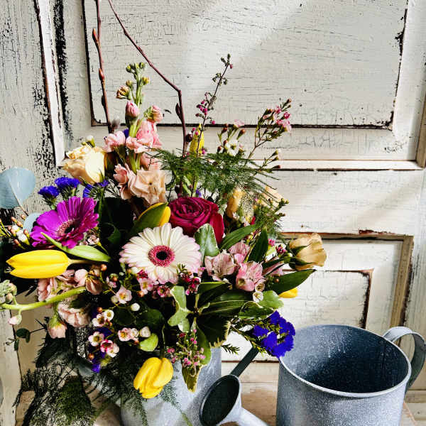 Mixed bouquet in a metal watering can with pink, yellow, white, and purple flowers