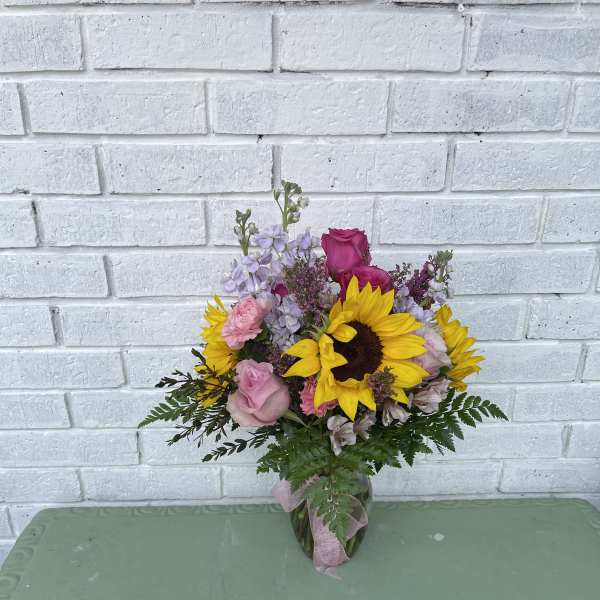 Bouquet of sunflowers, pink roses, and lavender flowers in a glass vase
