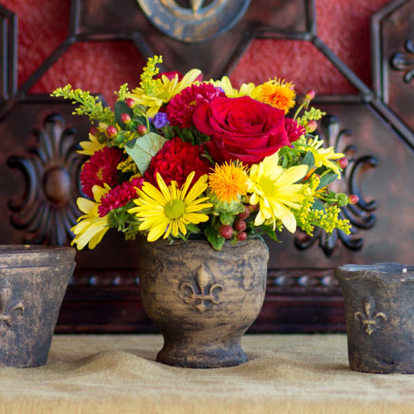 Mixed bouquet of red, yellow, and orange flowers in a rustic vase